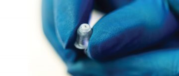 A microneedle is held by a hand in a blue glove