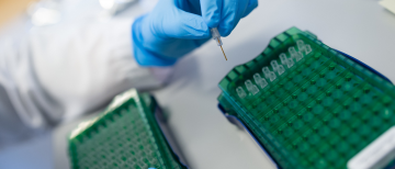 A person wearing gloves places a sample in a microwell plate