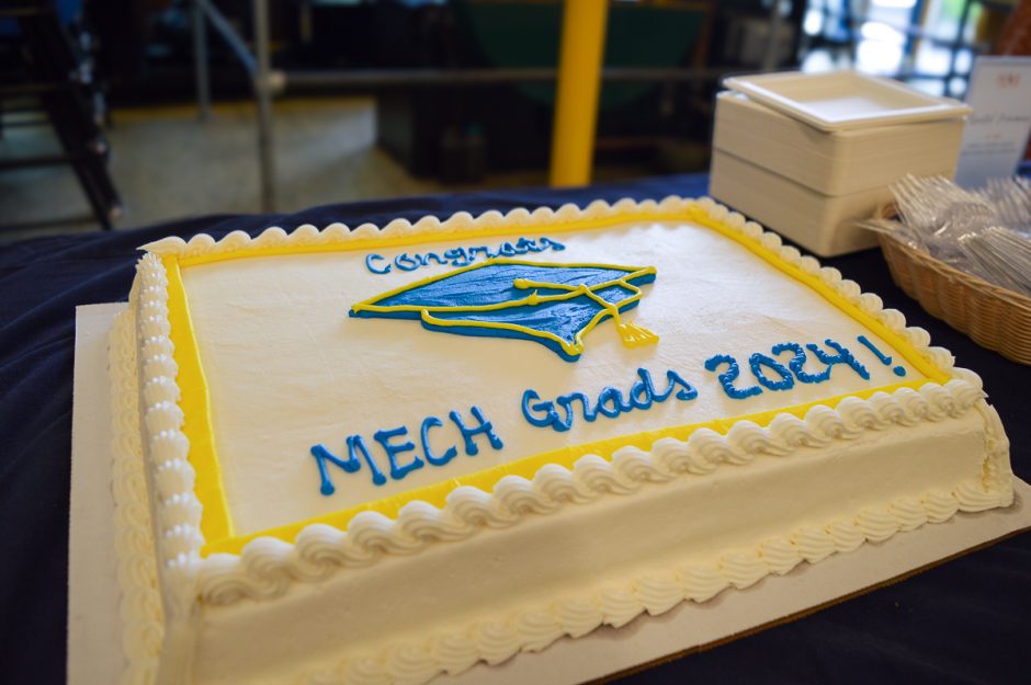 A graduation cake with the message "Congrats MECH Grads 2024! in blue and yellow icing.